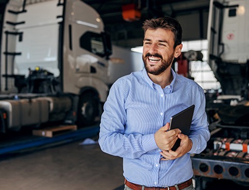 IMAGE: Man in truck bay smiling and looking away, holding tablet.