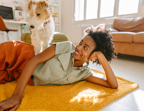 IMAGE: woman laying on a rug inside her house while a dog stands on her