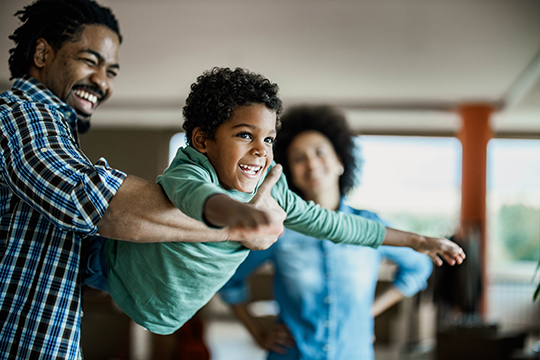 IMAGE: Man swinging son inside home while woman looks on smiling