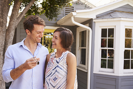IMAGE: Couple standing outside in front of home with man holding keys