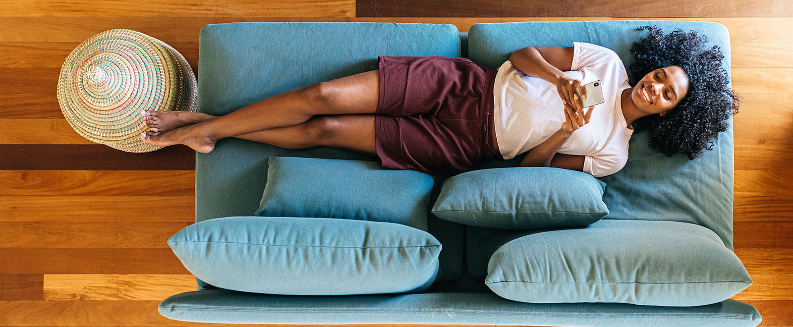 IMAGE: overhead shot of woman laying on couch smiling looking at phone.