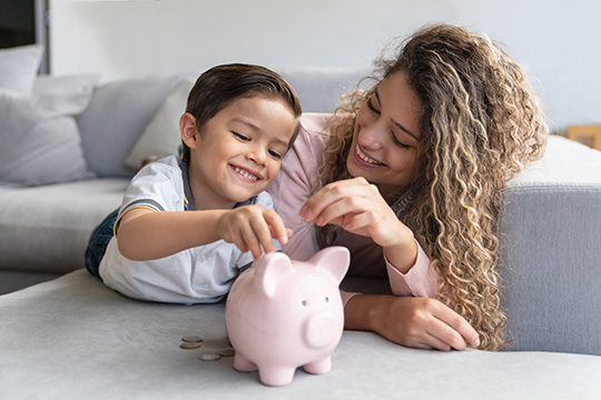 IMAGE: Mom and son laying on a couch together putting coins into a piggy bank