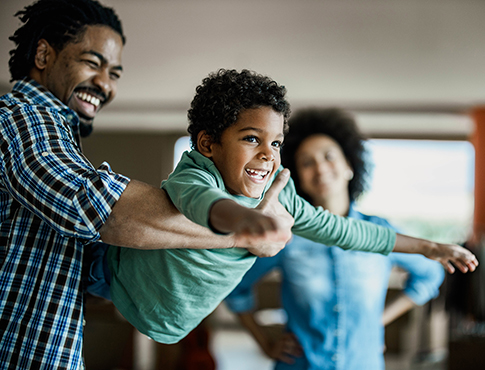 IMAGE: Father swinging kid in his arms while spouse looks on in background.