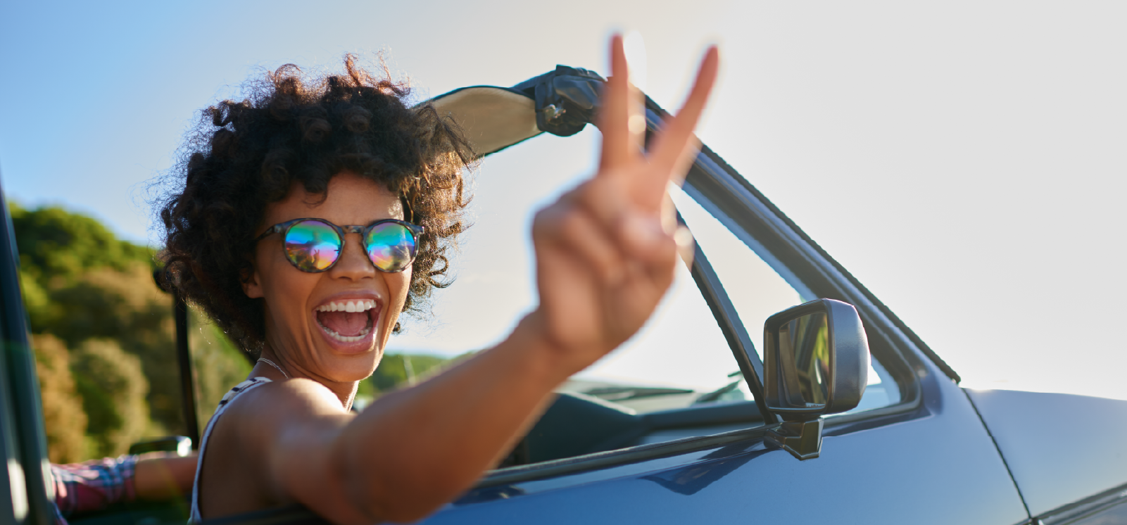 IMAGE: Woman in car smiling and giving peace sign