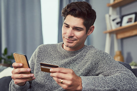 IMAGE: Man holding credit card and phone smiling