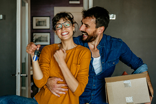 IMAGE: Smiling couple moving into new home with woman holding keys