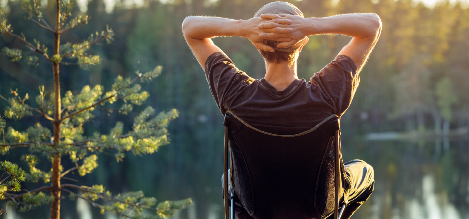 IMAGE: Back of a person sitting beside a lake with hands behind their head