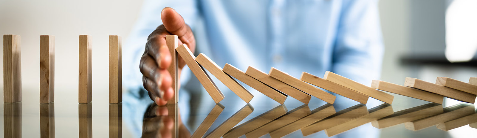 IMAGE: Wooden dominoes falling on table with hand stopping the progression.