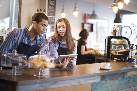 IMAGE: Coworkers looking at tablet together inside a cafe