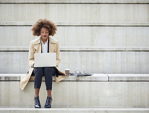 IMAGE: Woman sitting outside and smiling while working on a laptop