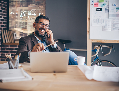 IMAGE: Mature male in sport coat on phone at laptop.