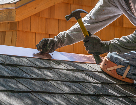 IMAGE: Closeup of roofer tapping nail into flashing on roof