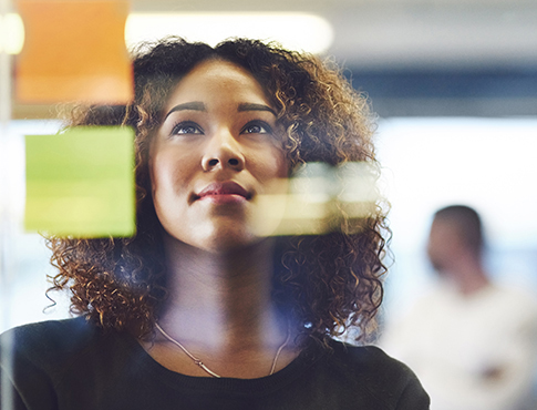 IMAGE: Woman standing at glass window, looking up at colorful post-it notes