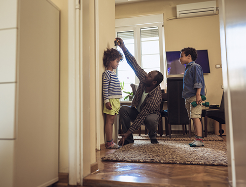 IMAGE: Father measuring the height of a child with another child watches.