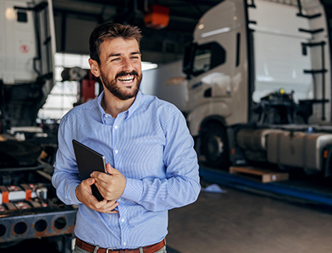 IMAGE: Man in truck bay smiling and looking away, holding tablet.