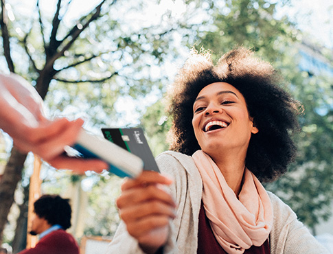 IMAGE: Woman outdoors paying with credit card by tapping card on payment tablet.