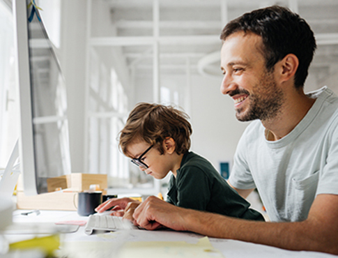 IMAGE: Man sitting at computer with young son on his lap watching.