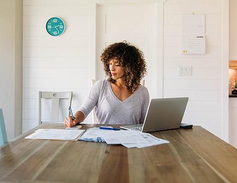 IMAGE: Woman at table with laptop making notes.