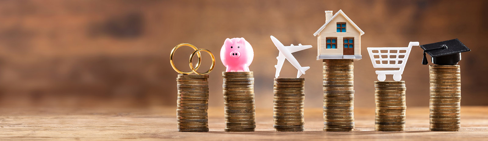 IMAGE: Six stacks of coins, left to right topped with two wedding rings, piggy bank, airplane, home, shopping cart, graduation cap.