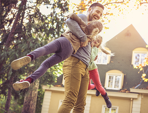 IMAGE: Father playing with his daughters in the yard of their home.