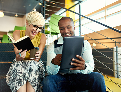 IMAGE: Woman and man business colleagues sitting on stairs in office comparing notes.